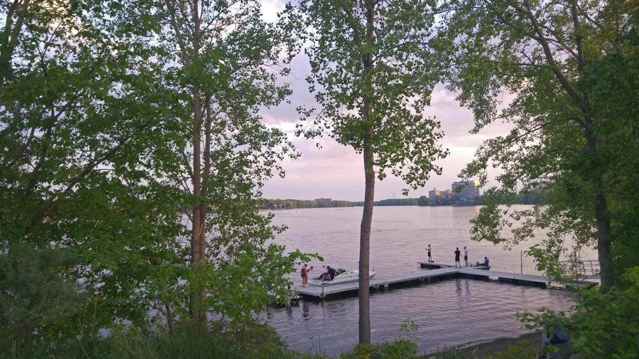 People on a dock at the water's edge on a summer evening, framed by trees