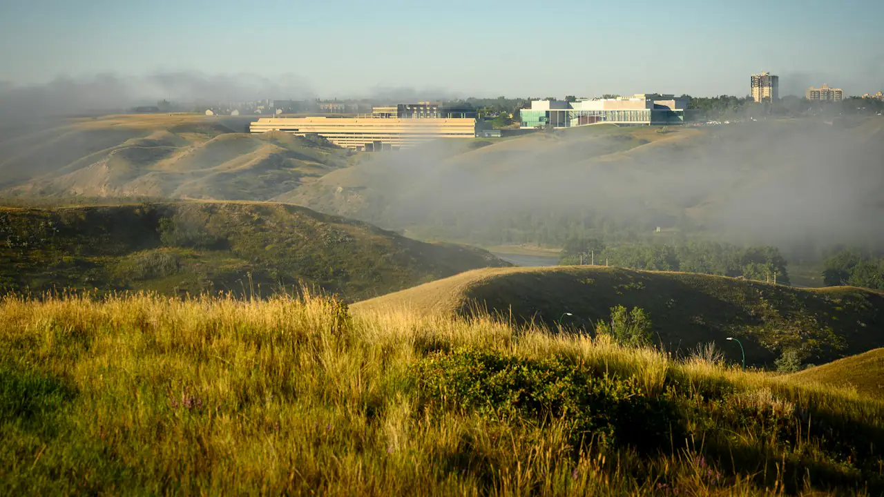 Morning fog lifting off the grassy coulees, with the University of Lethbridge along the ridge