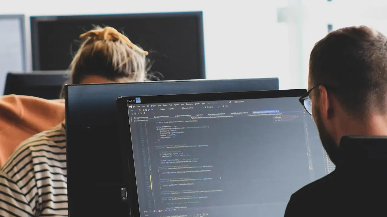 Two developers working on code at large monitors in a bright office