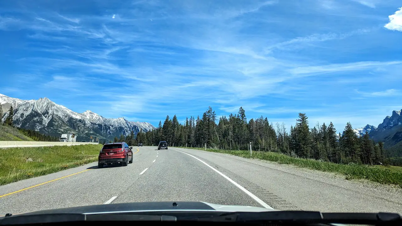 A red car on the Trans Canada Highway heading toward the Rocky Mountains under a blue sky