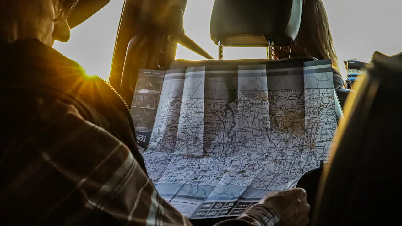 A driver studying a paper road map behind the wheel as the sun comes through the windshield