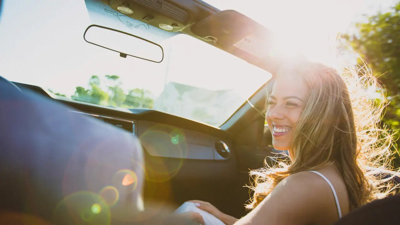 A smiling woman in the passenger seat of a car in warm afternoon light