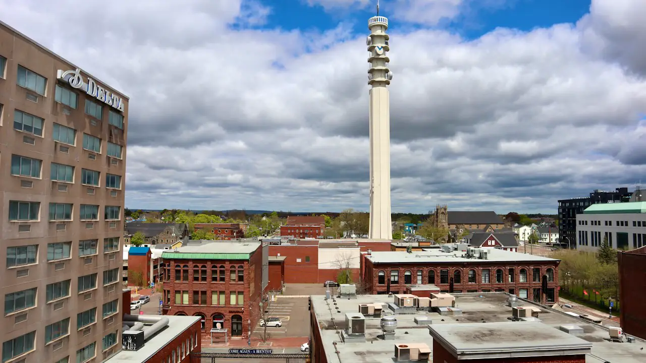 Downtown Moncton's brick buildings around a tall white tower under a bright, cloudy sky