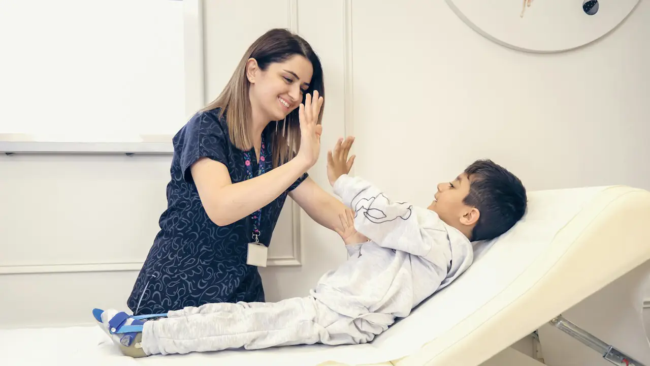 A smiling nurse giving a high five to a young patient sitting up in bed