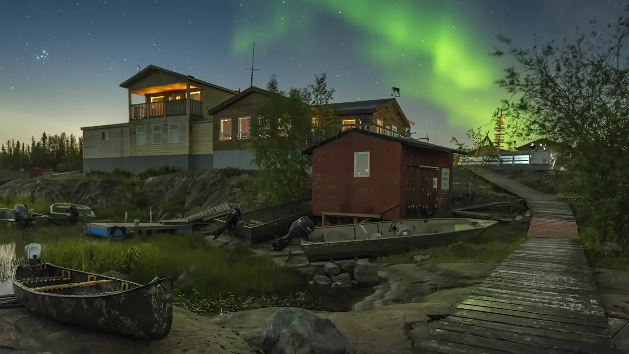 Green northern lights over lakeside houses and a boardwalk in Yellowknife
