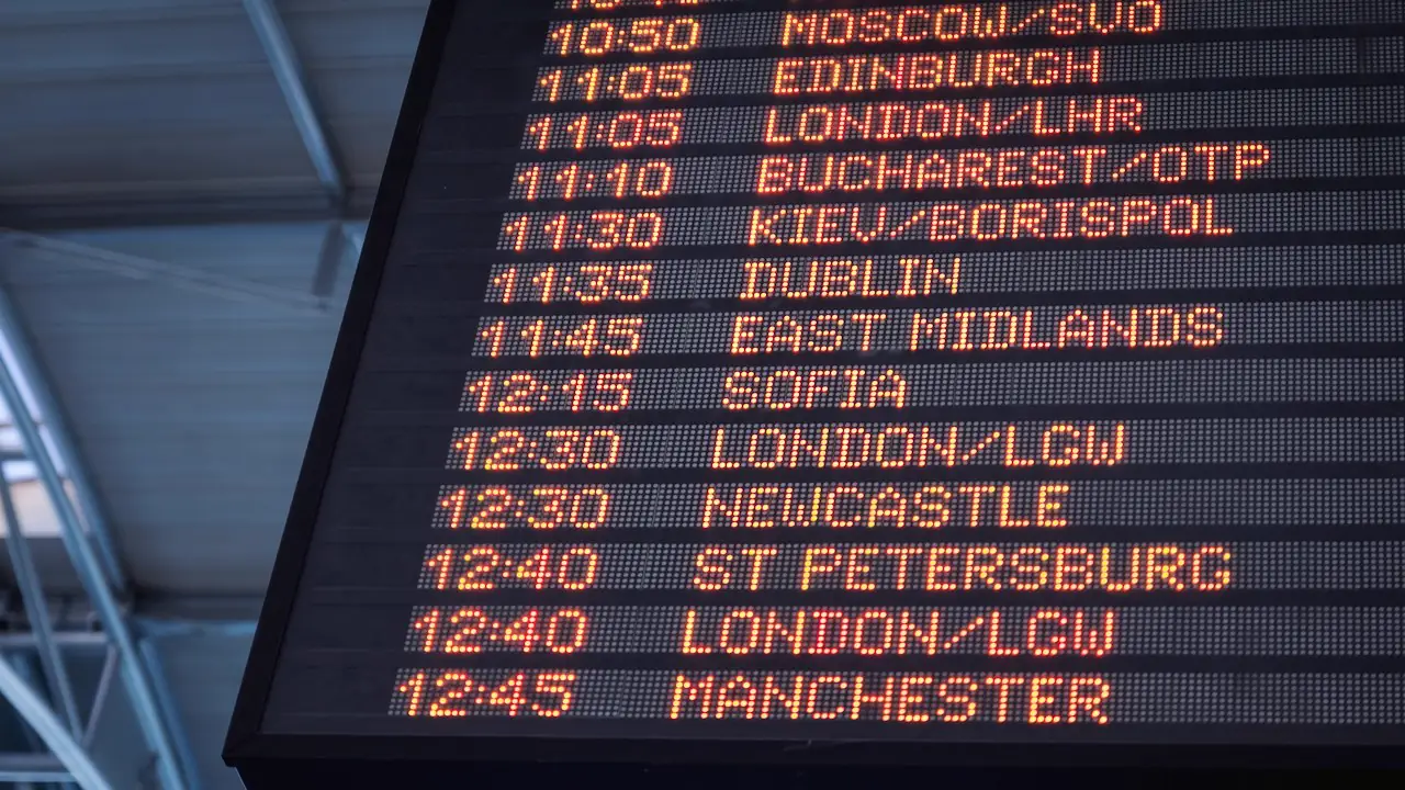 An airport departure board listing flights to cities across Europe