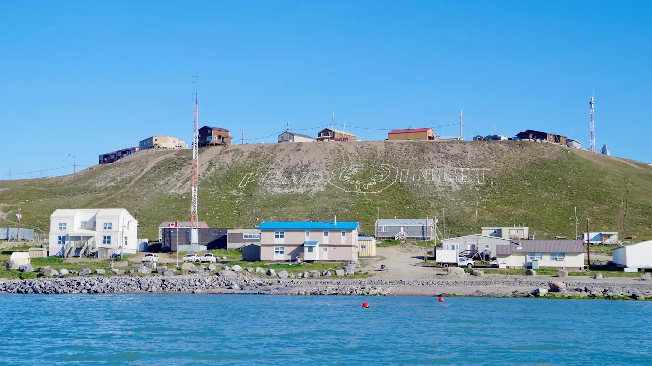 Houses of an Arctic community at the foot of a hill beside blue water in summer