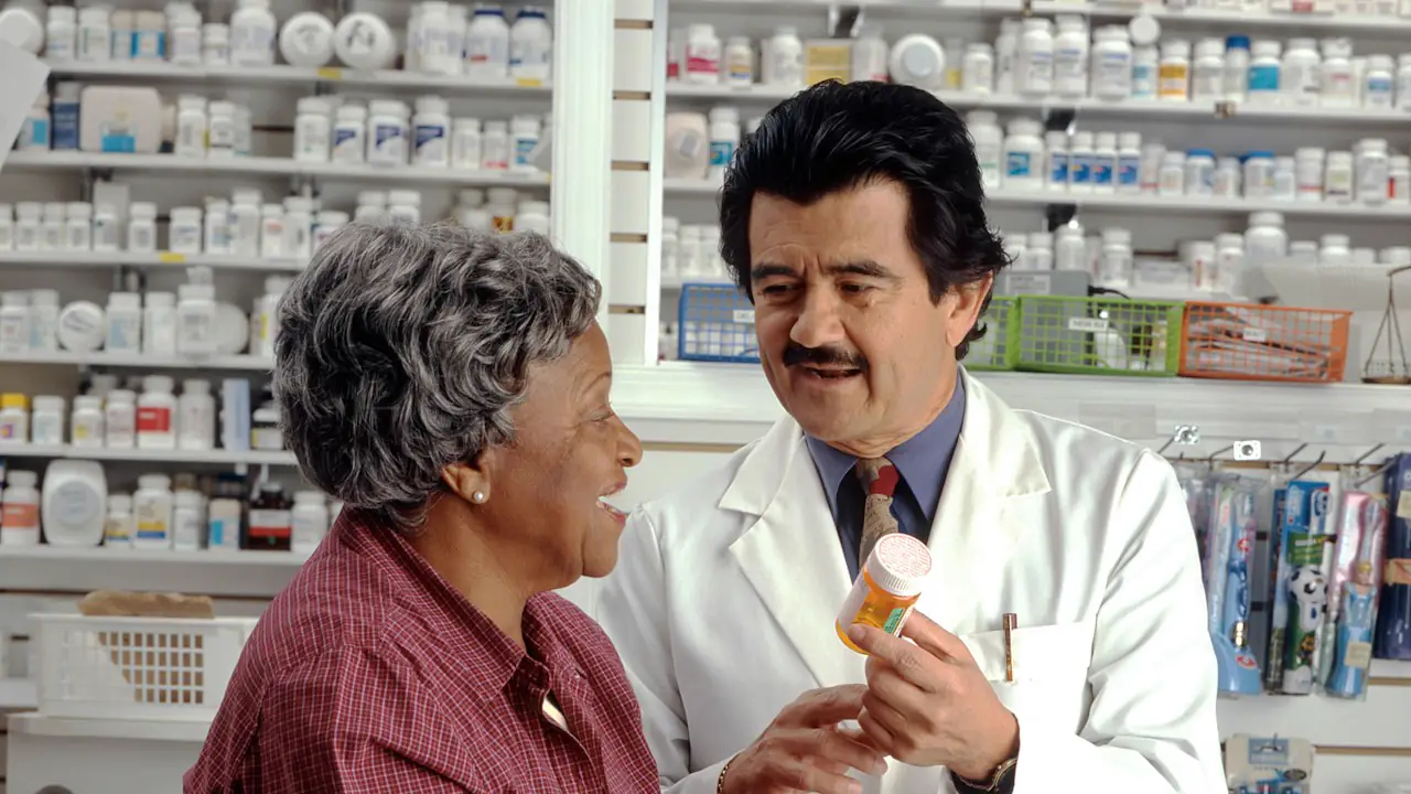 A pharmacist in a white coat explaining a prescription to a smiling customer