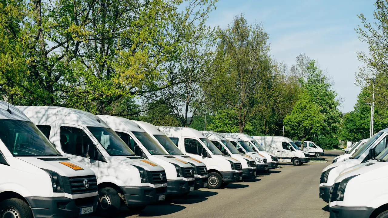 A row of white delivery vans parked along a tree lined road