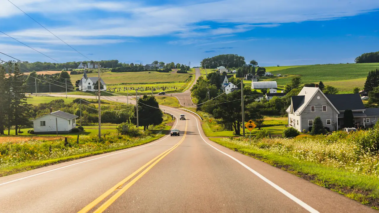 A country road running between green farm fields and houses on the Island