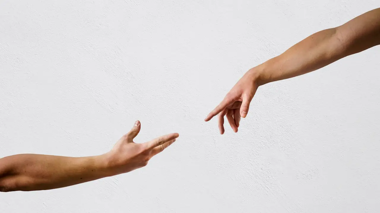 Two hands reaching toward each other against a pale background