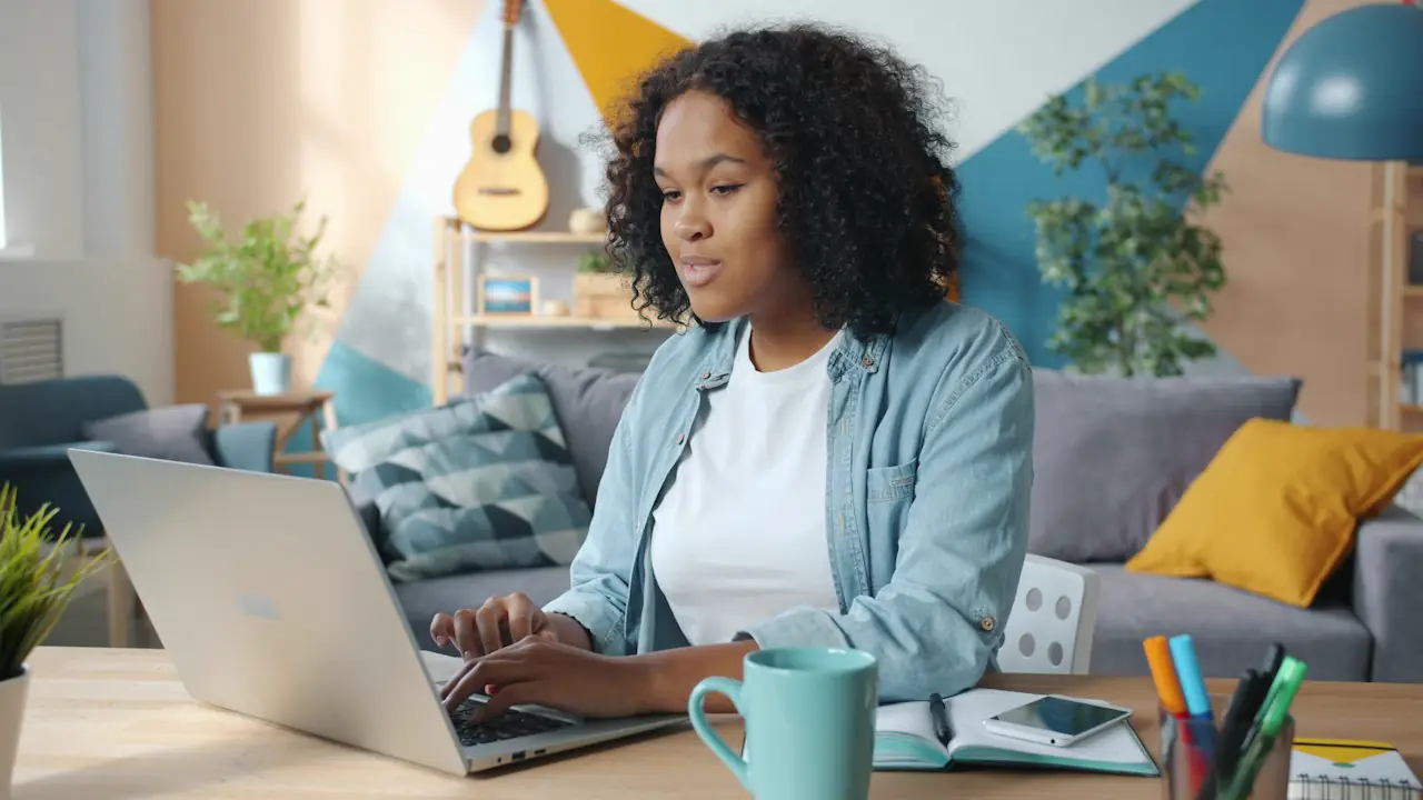 A smiling woman working on a laptop at a desk in a bright home office