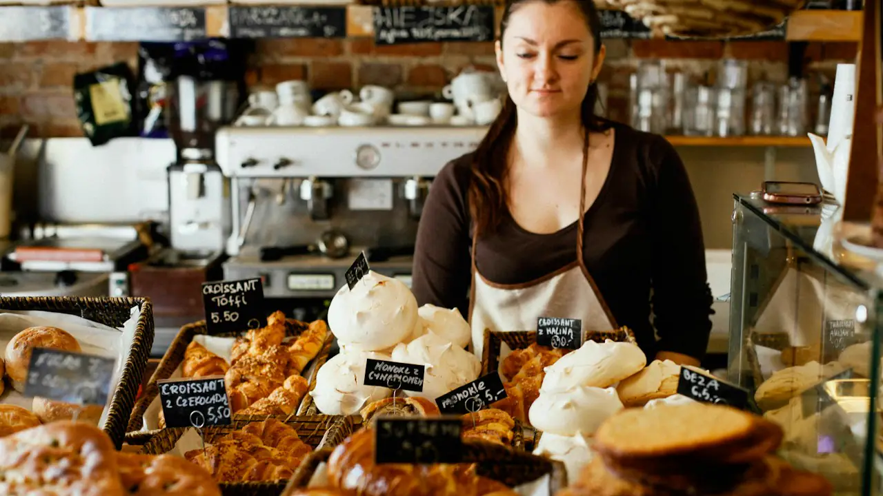 A baker behind a counter of fresh pastries and meringues in a small shop