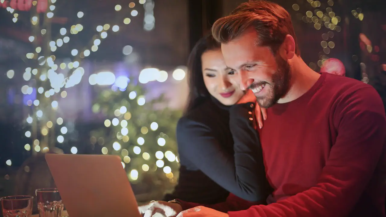 A couple smiling at a laptop together in a warmly lit room