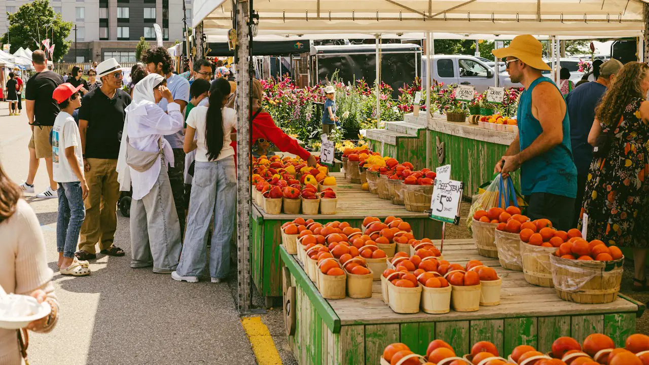 Shoppers at an outdoor market stall piled with tomatoes and flowers