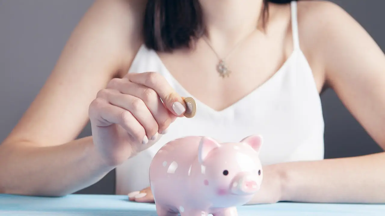 A woman dropping a coin into a pink piggy bank