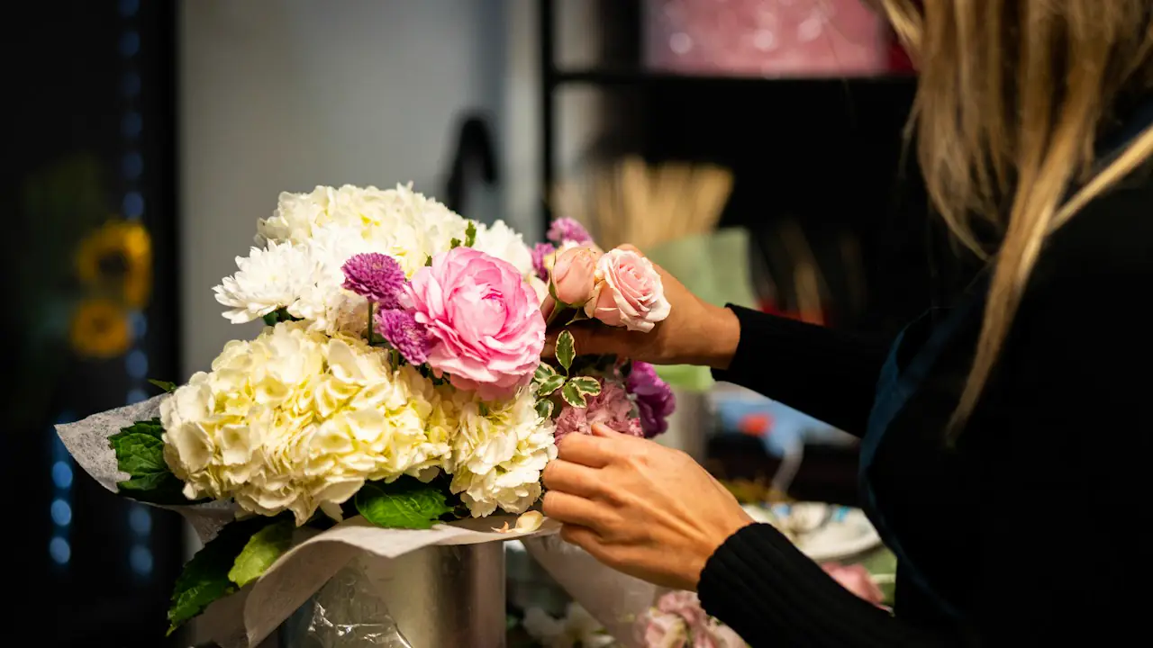 A florist arranging pink and white flowers into a bouquet