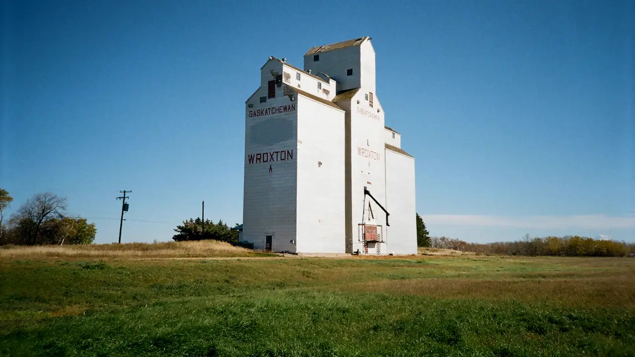 A white wooden grain elevator standing alone on the prairie under a deep blue sky