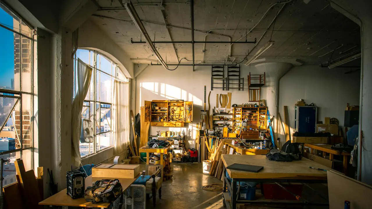 A workshop full of tools and workbenches lit by tall windows