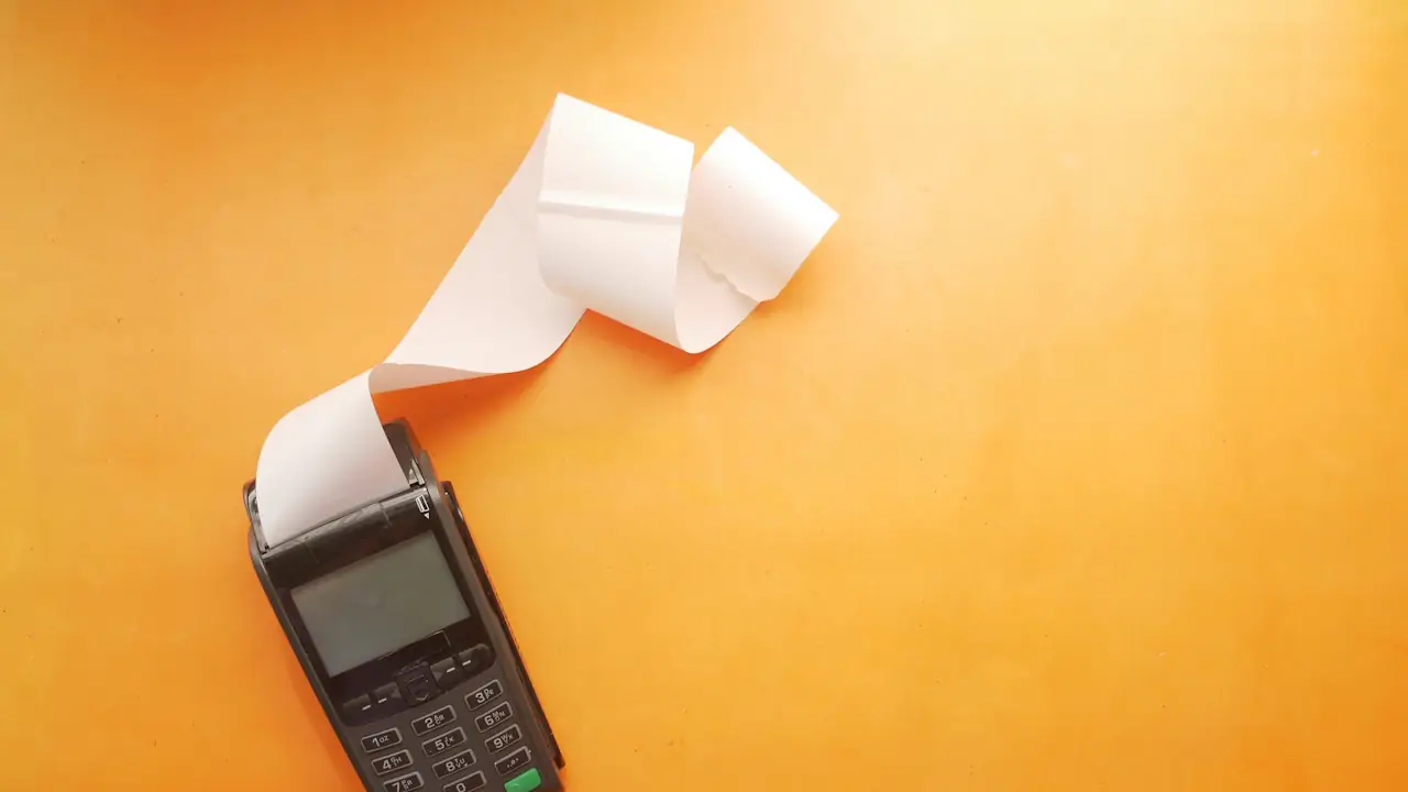 A card payment terminal printing a receipt on an orange background