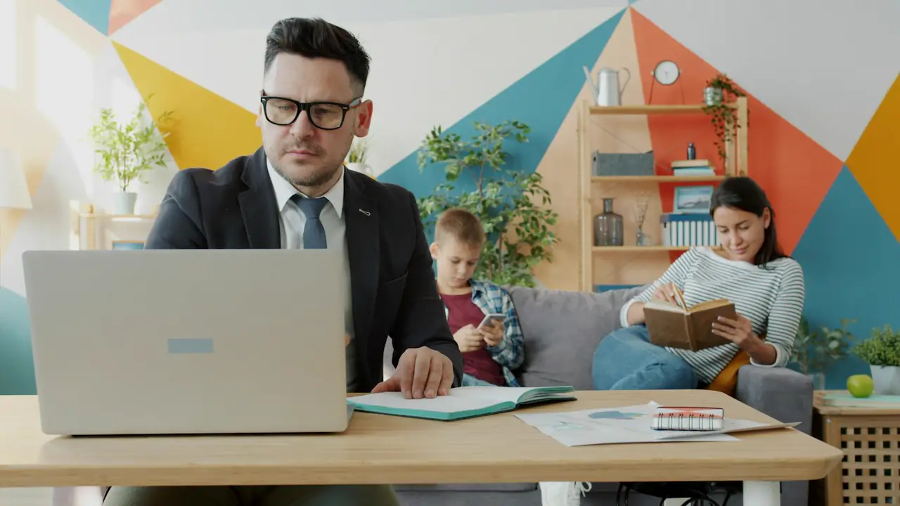 A man working on a laptop at home while his family relaxes behind him