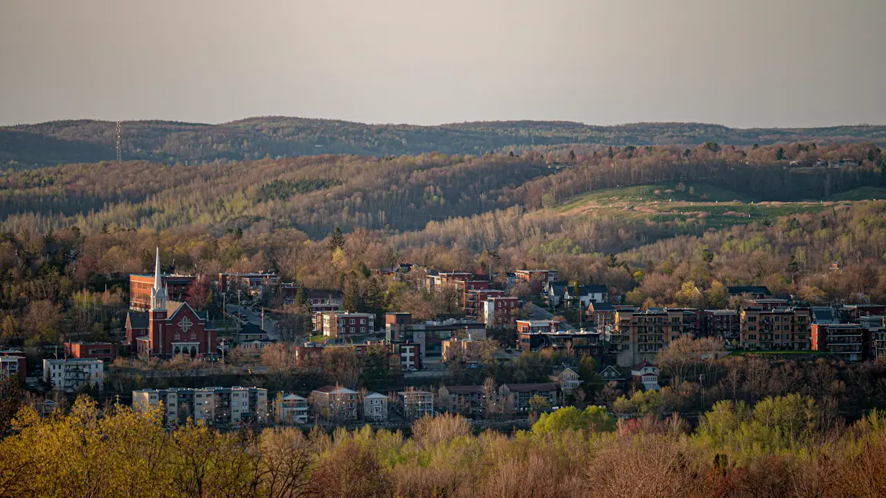 Sherbrooke's rooftops and church spire in a valley of autumn trees