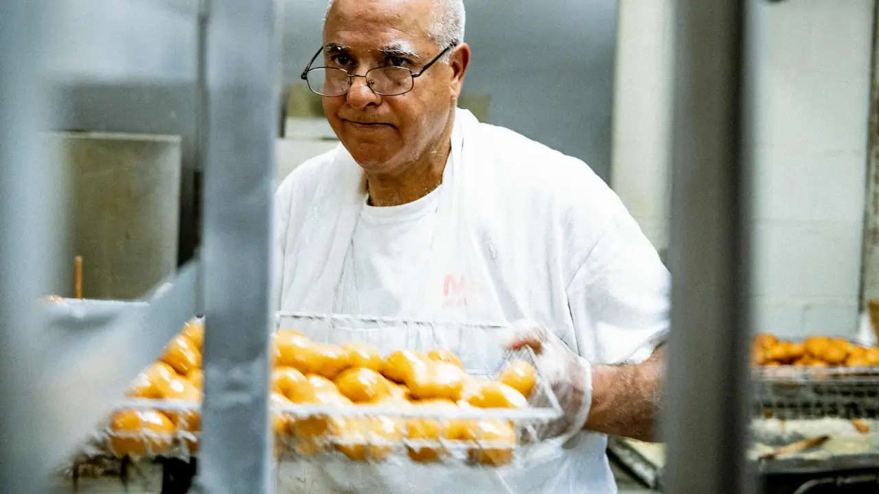 A baker holding a tray of fresh buns in a commercial kitchen