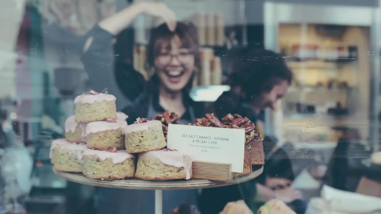 A smiling bakery owner behind a display of cakes
