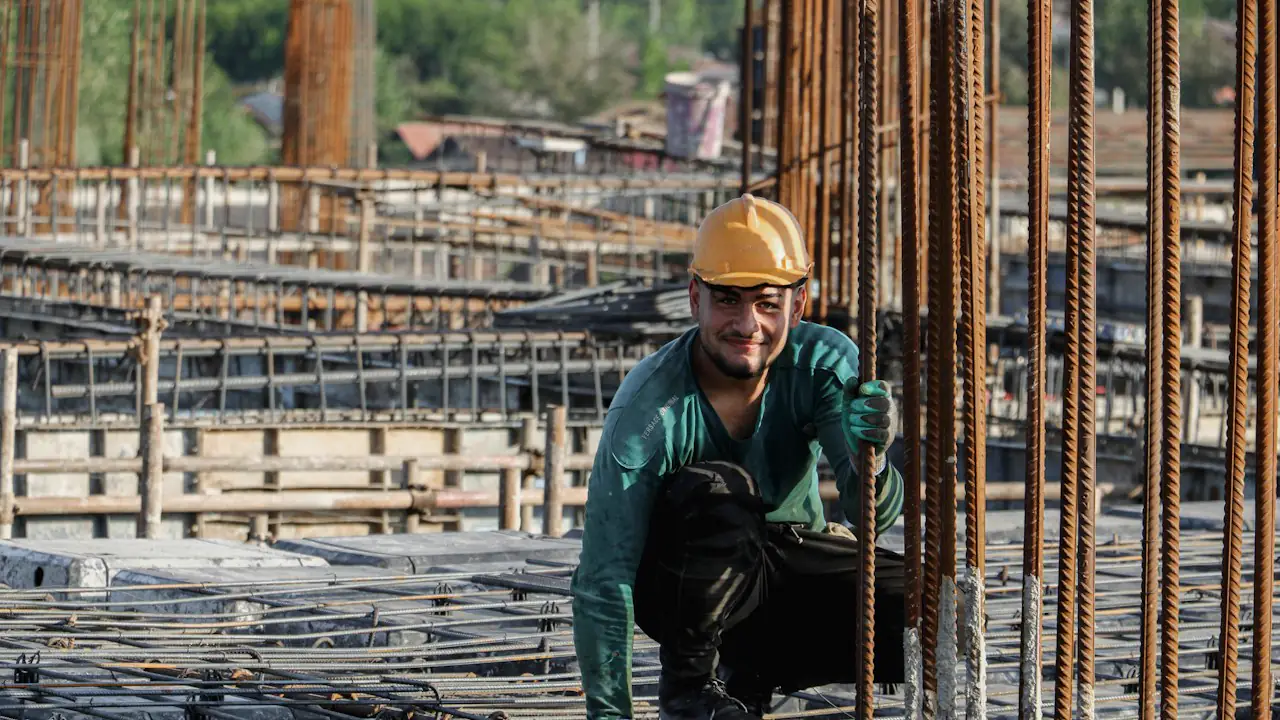 A smiling construction worker in a hard hat kneeling among rebar on a building site