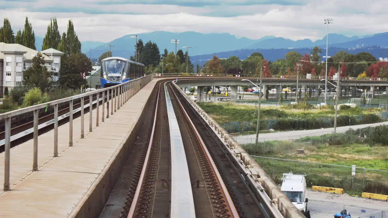 An elevated SkyTrain line in Metro Vancouver with a train approaching and mountains behind