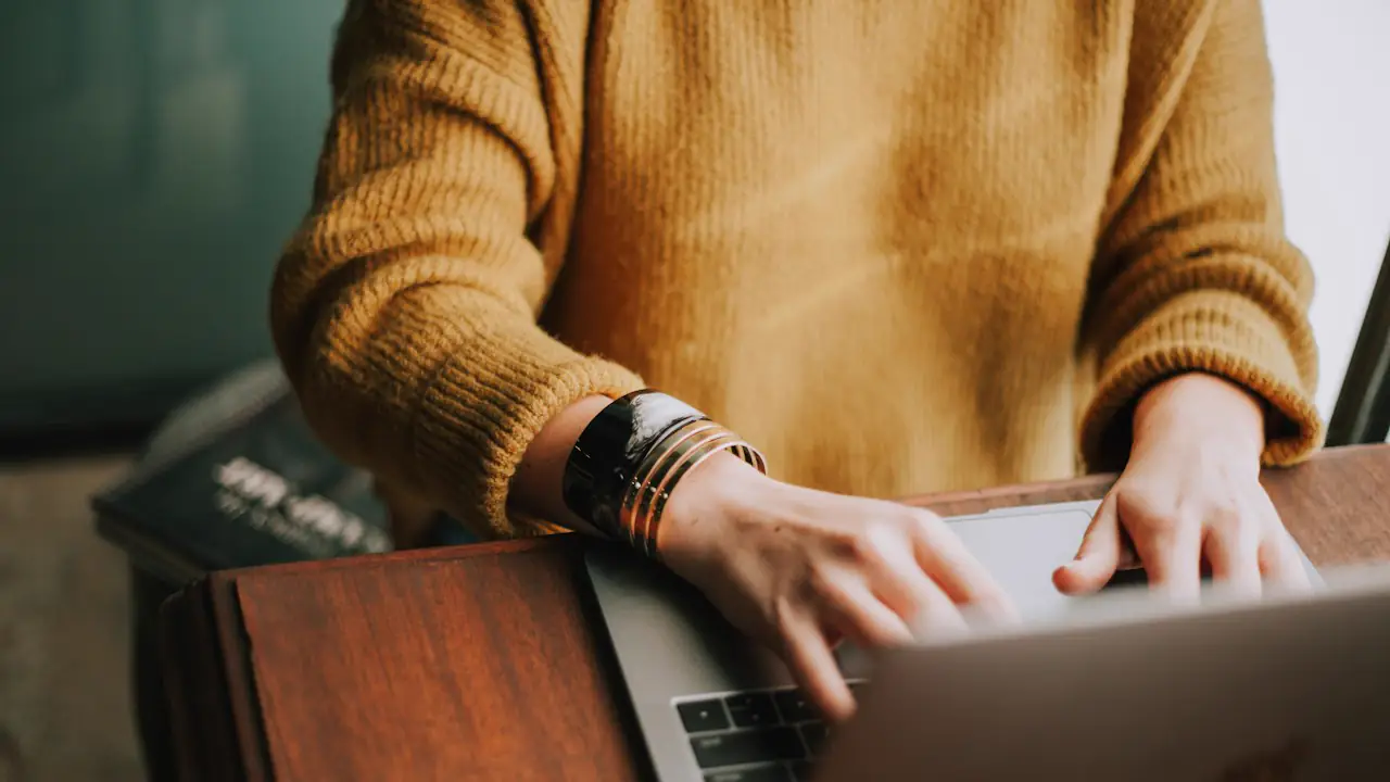 Hands typing on a laptop at a wooden desk