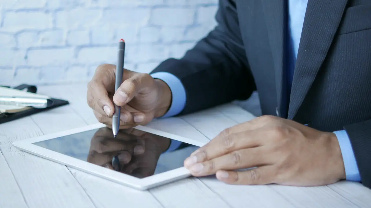 A man in a suit signing a document on a tablet with a stylus