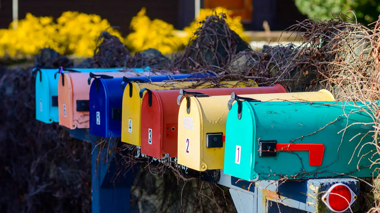 A row of brightly painted mailboxes on a post beside a garden