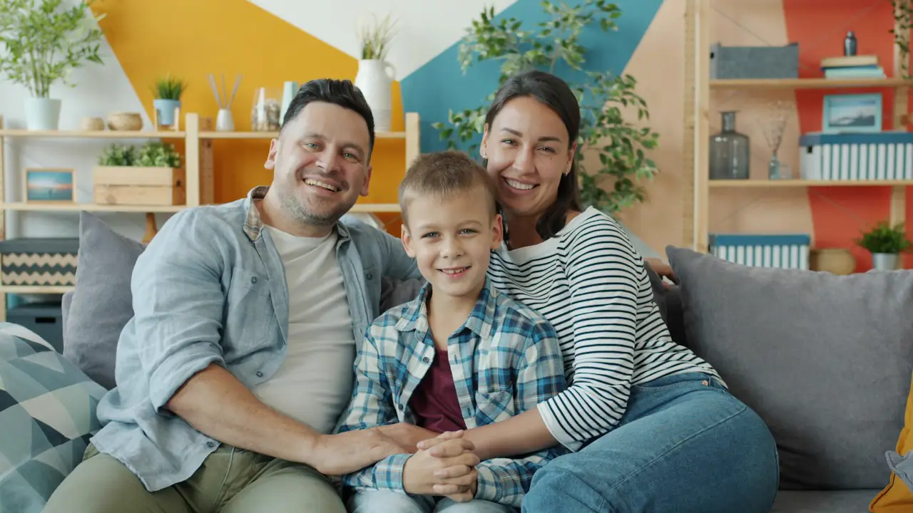 A smiling mother, father and young son sitting together on a sofa at home