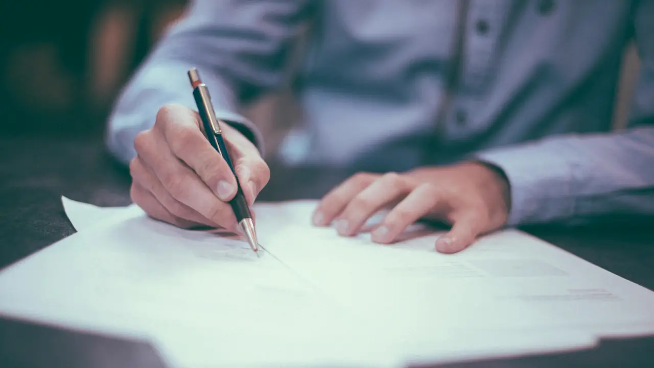 A hand signing a document with a pen on a desk