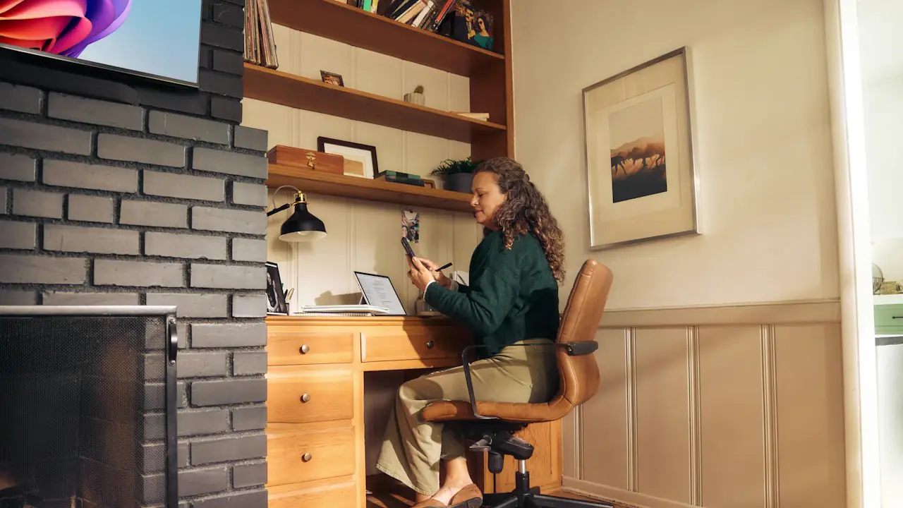 A woman working at a wooden desk in a cosy home office lined with shelves