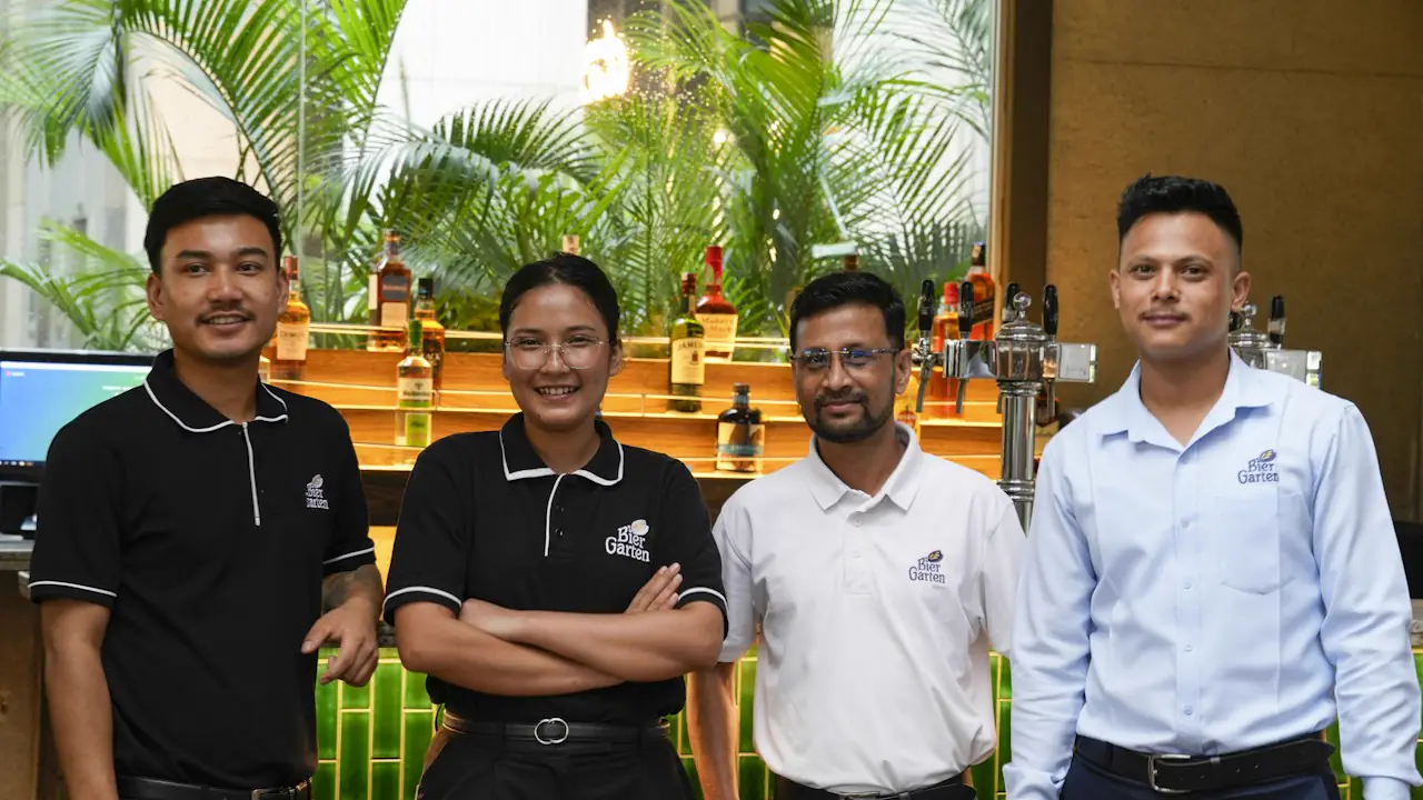 Four smiling restaurant staff in uniform standing together in front of the bar