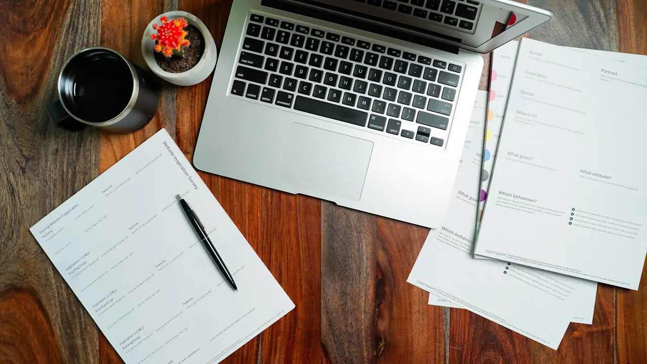 A laptop, notepad and payroll papers on a wooden desk