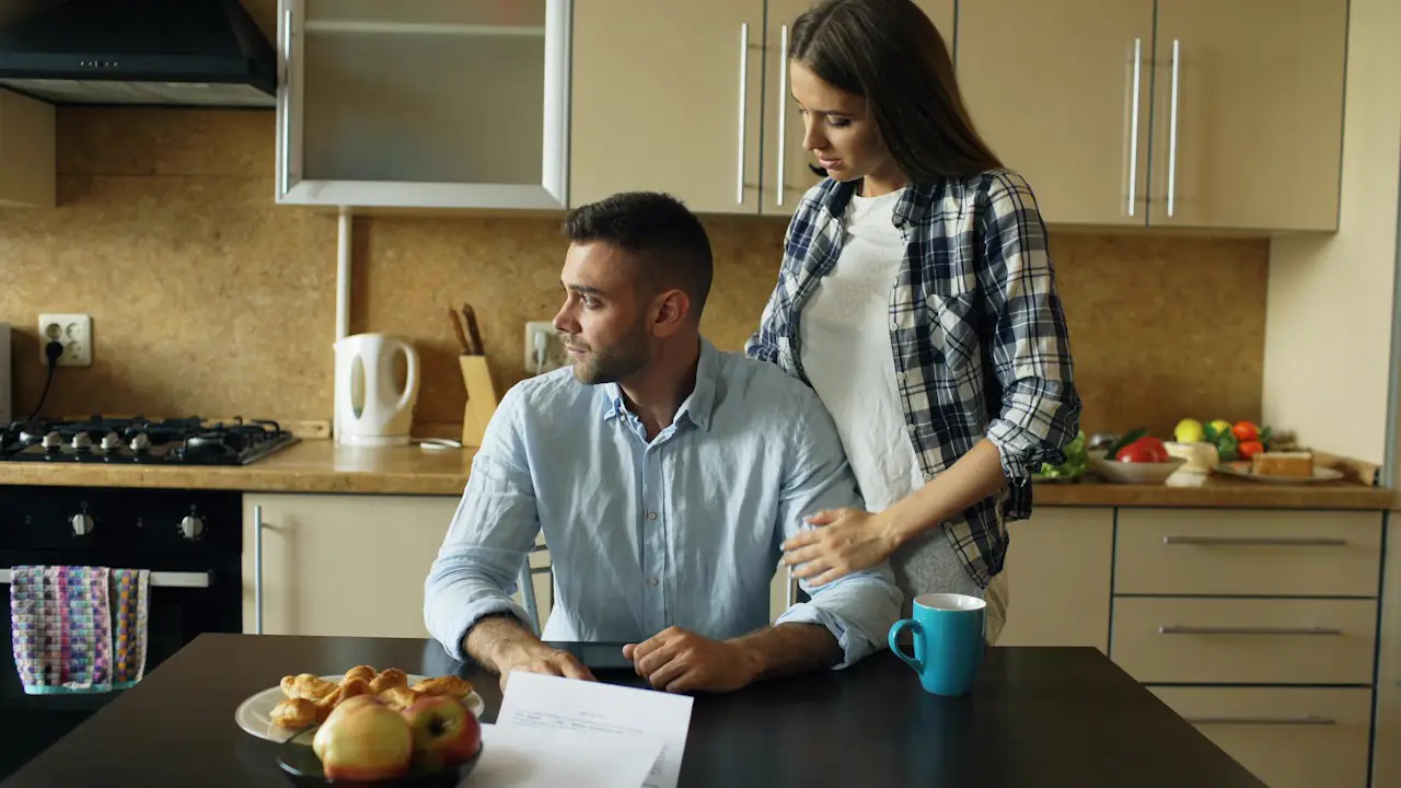 A couple at a kitchen table looking over a printed statement together