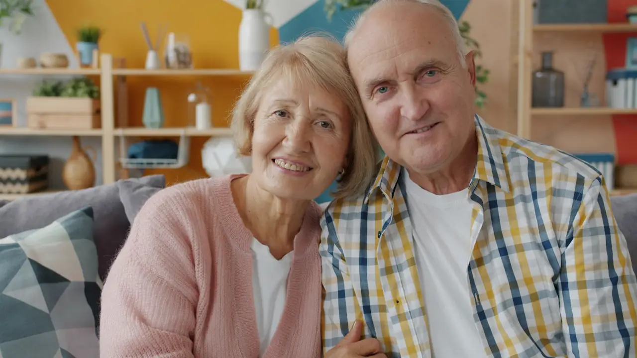 A smiling older couple sitting close together on a sofa at home