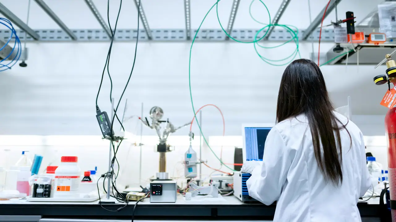 A scientist in a lab coat working at a bench crowded with research equipment