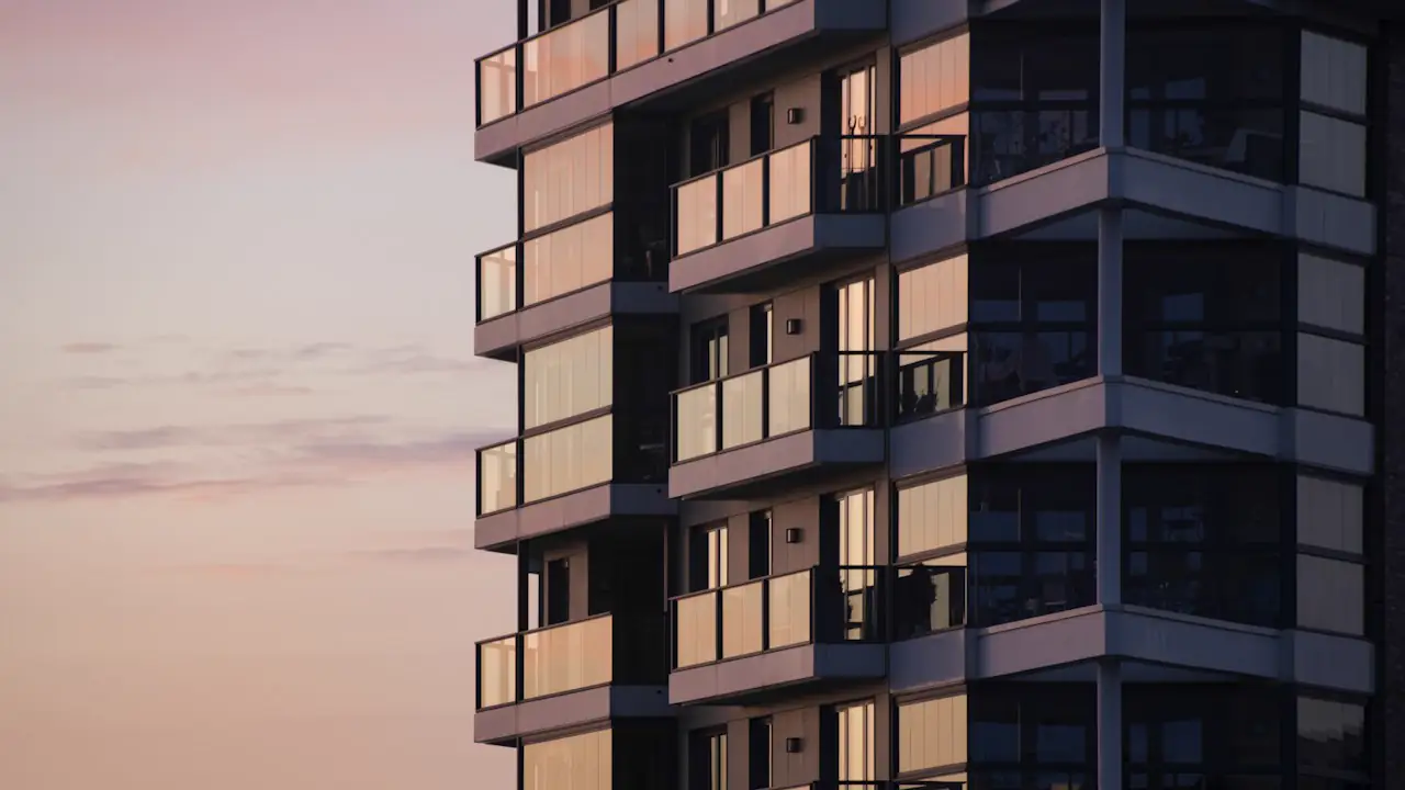 An apartment building with glass balconies against a soft evening sky