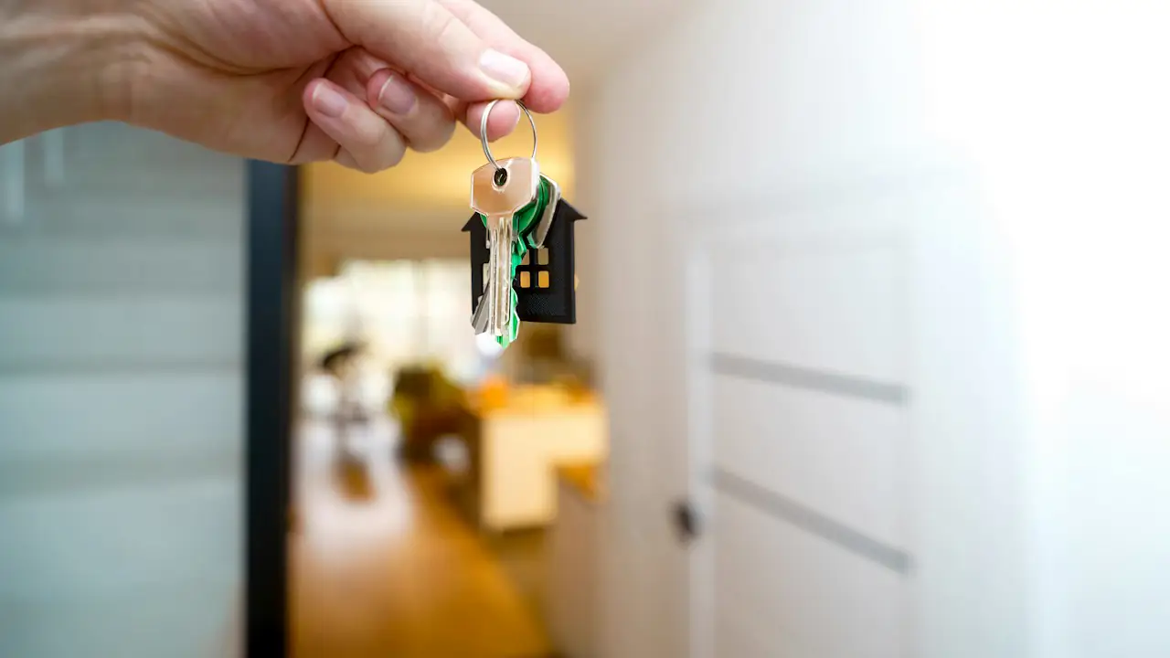 A hand holding a set of house keys inside the doorway of a bright home