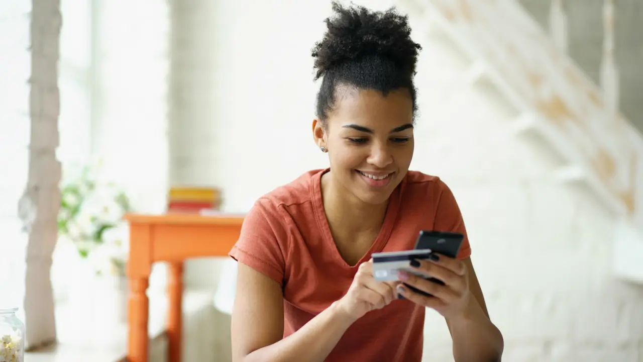 A young woman smiling as she pays with her phone and a bank card