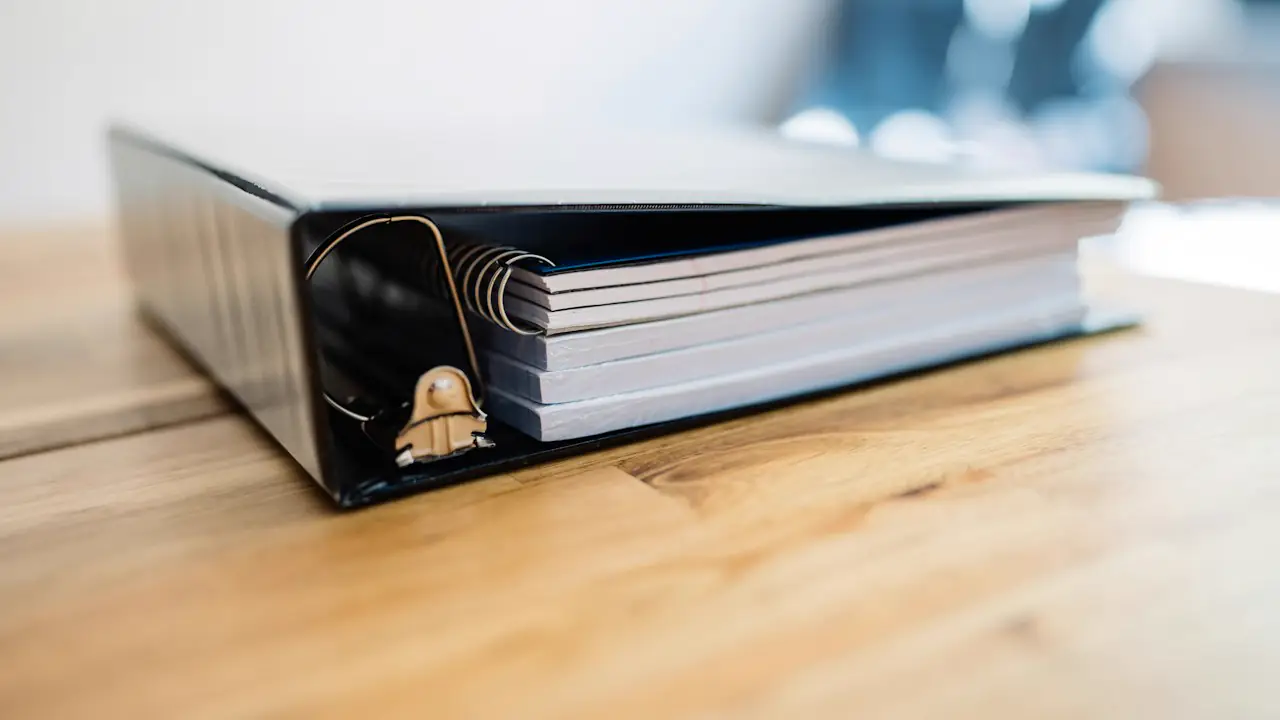 A thick ring binder on a wooden desk