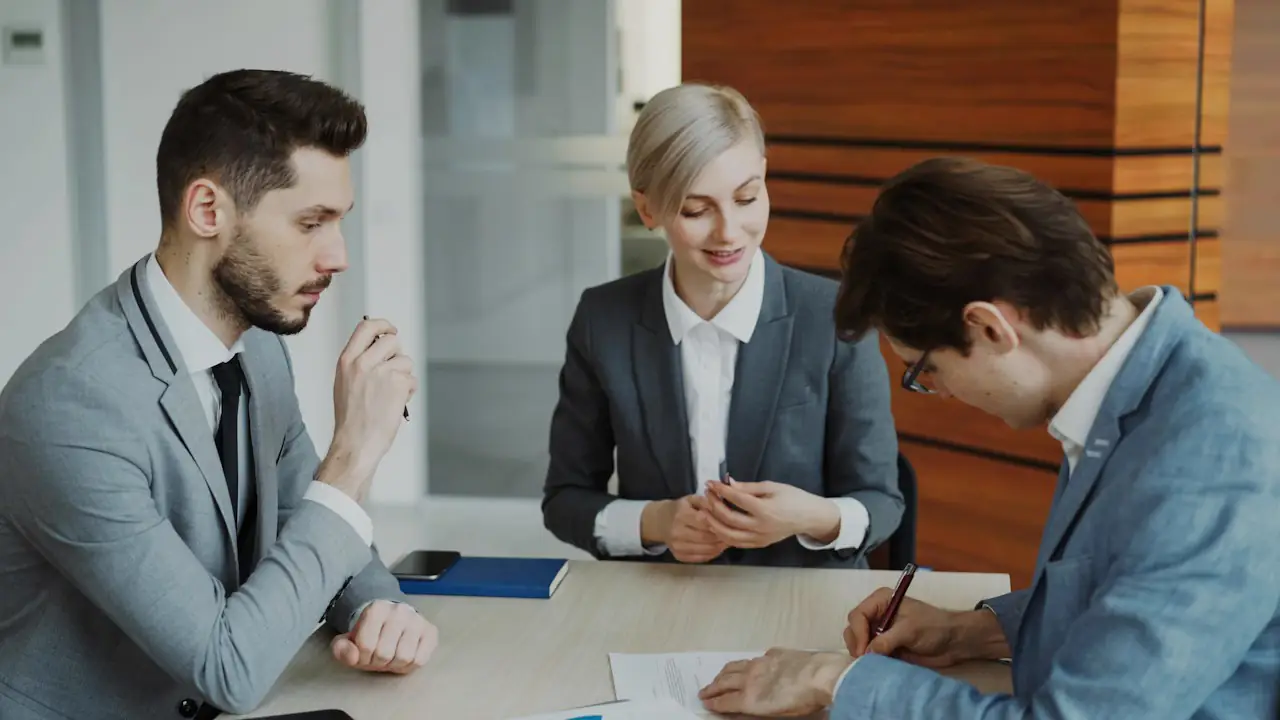 Three professionals at a table as one of them signs an agreement