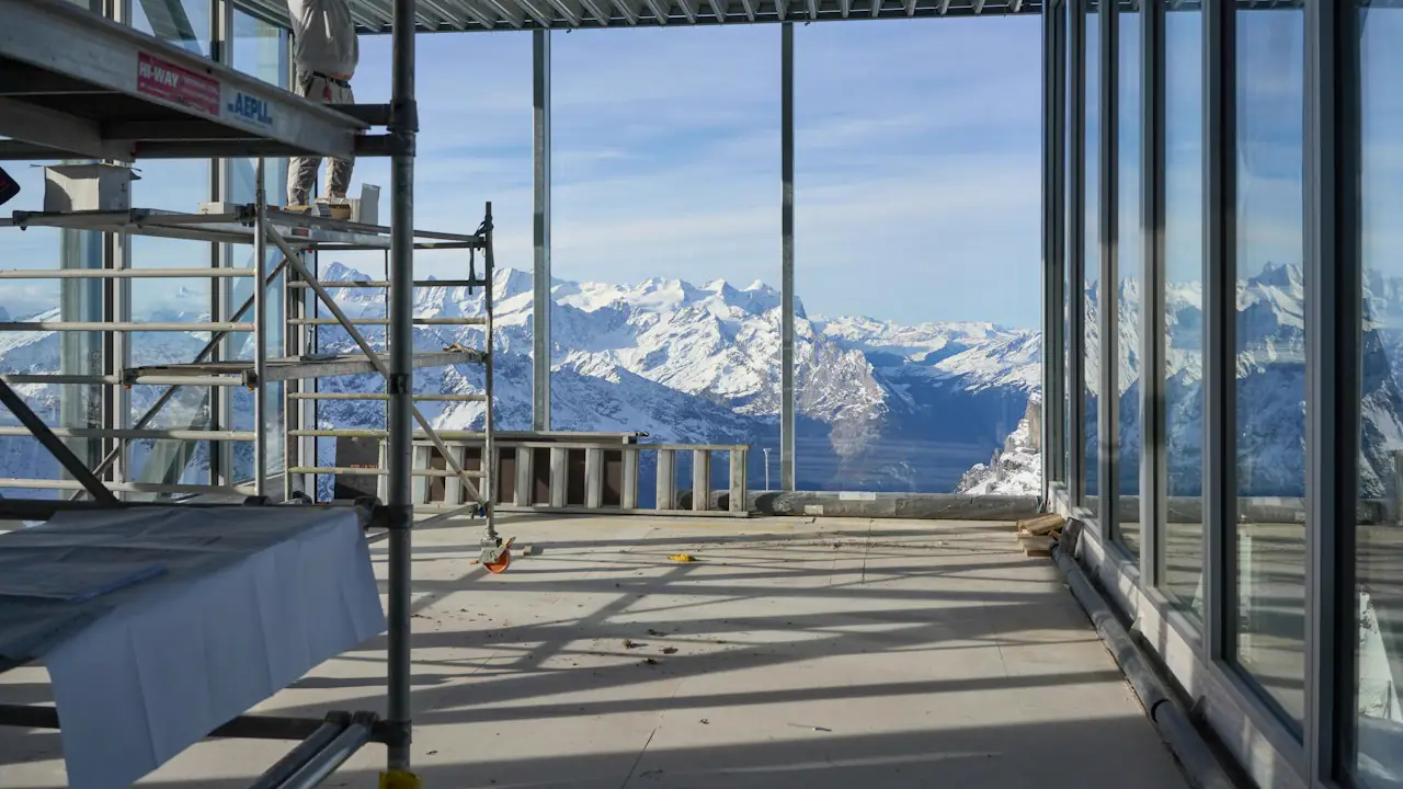 An unfinished building with tall windows looking out on snow covered mountains