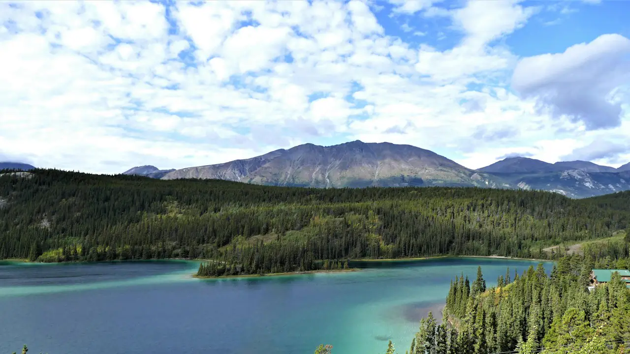 The green water of Emerald Lake below forested hills and mountains in the southern Yukon