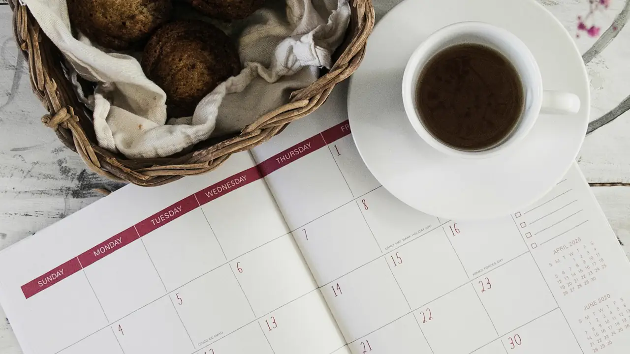 An open planner beside a cup of coffee and a basket