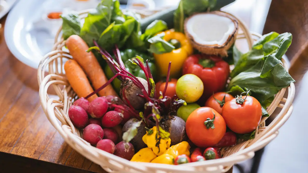 A wicker basket of fresh carrots, tomatoes, peppers, radishes and greens